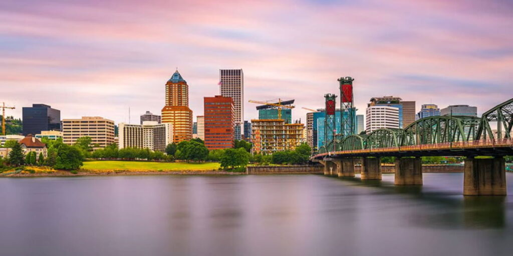 Portland skyline at sunset with the Hawthorne Bridge spanning the Willamette River, showcasing the urban environment where oregon solar incentives help businesses transition to renewable energy.