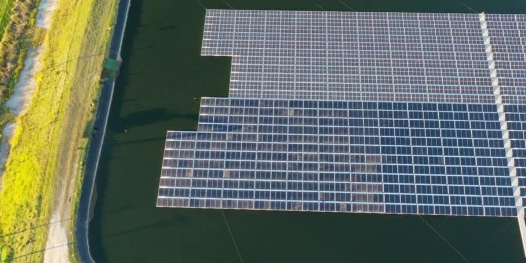 Aerial view of a floating solar panel array on a large body of water, surrounded by green vegetation
