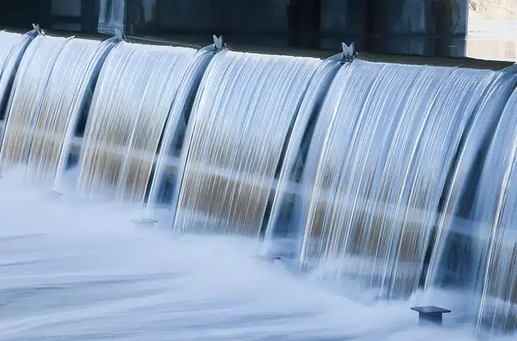 An illustration of hydropower, one of the primary types of green energy sources, showing water flowing through turbines to generate electricity