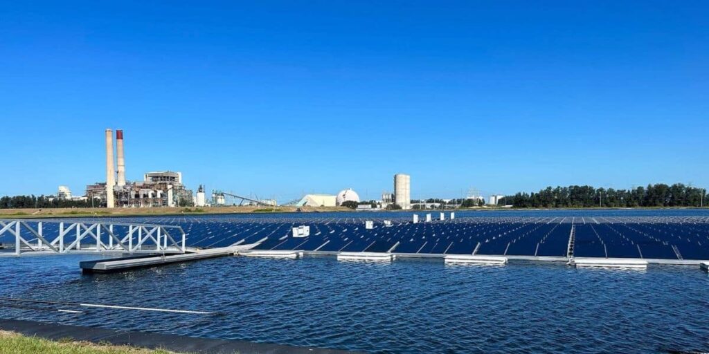 Floating solar panels on a reservoir with an industrial facility in the distance showing solutions to habitat loss through water based clean energy installations.